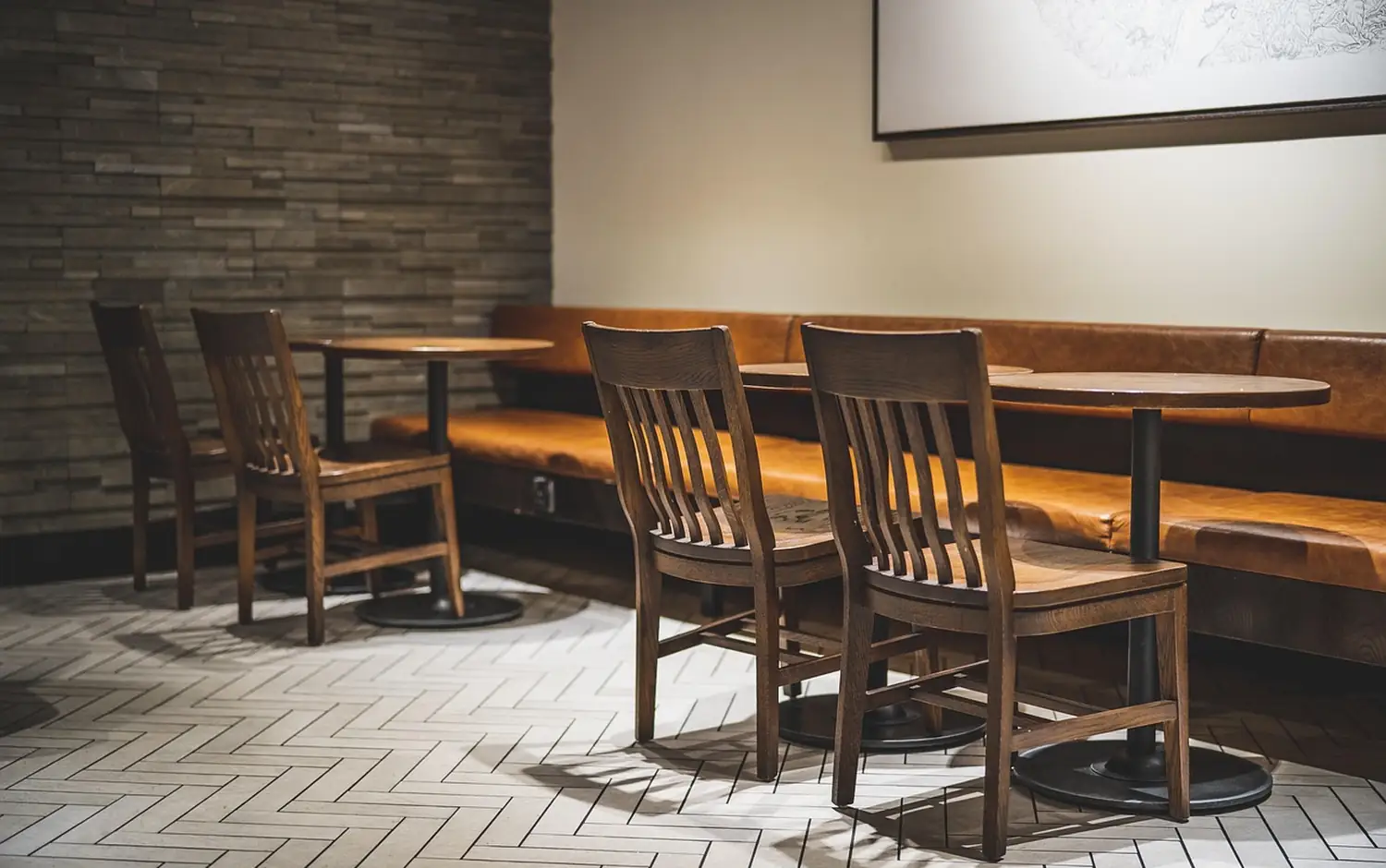 Inside the cafe: wooden chairs, a long banquette and tables along a herringbone floor