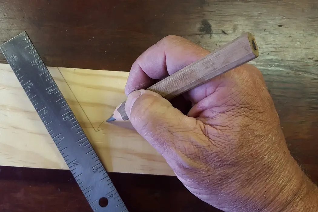A hand marking a pencil line on a board against a steel rule