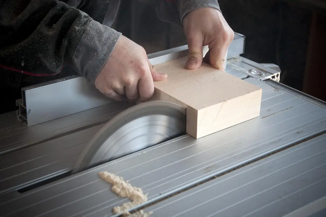 Hands feeding a length of timber through a bench saw