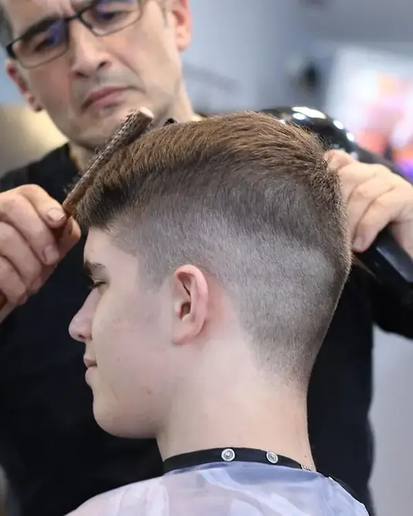 A barber finishing a skin fade with a comb and dryer